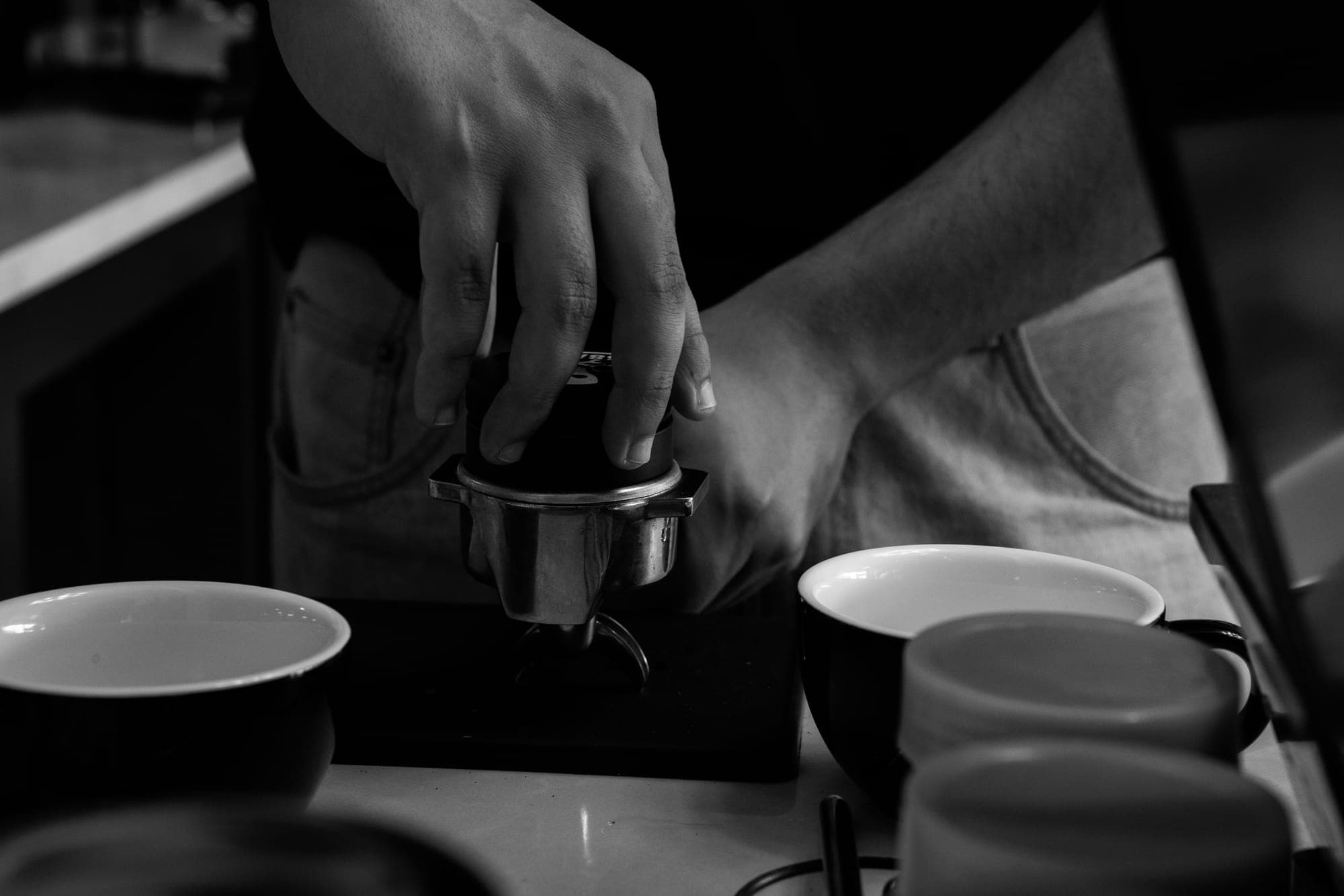 A barista tamping espresso, in black and white
