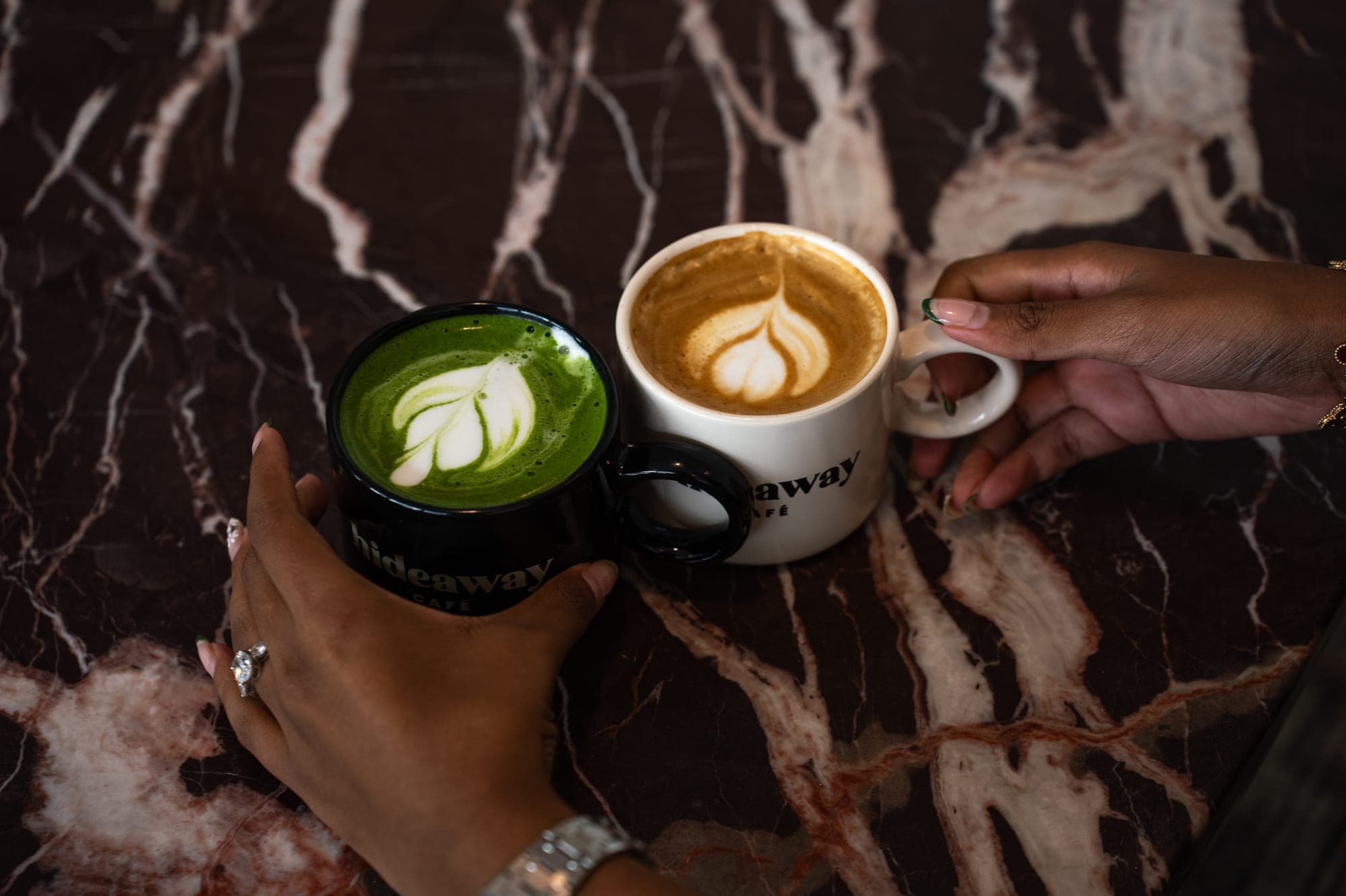 Two hands meeting over a matcha latte and a cappuccino